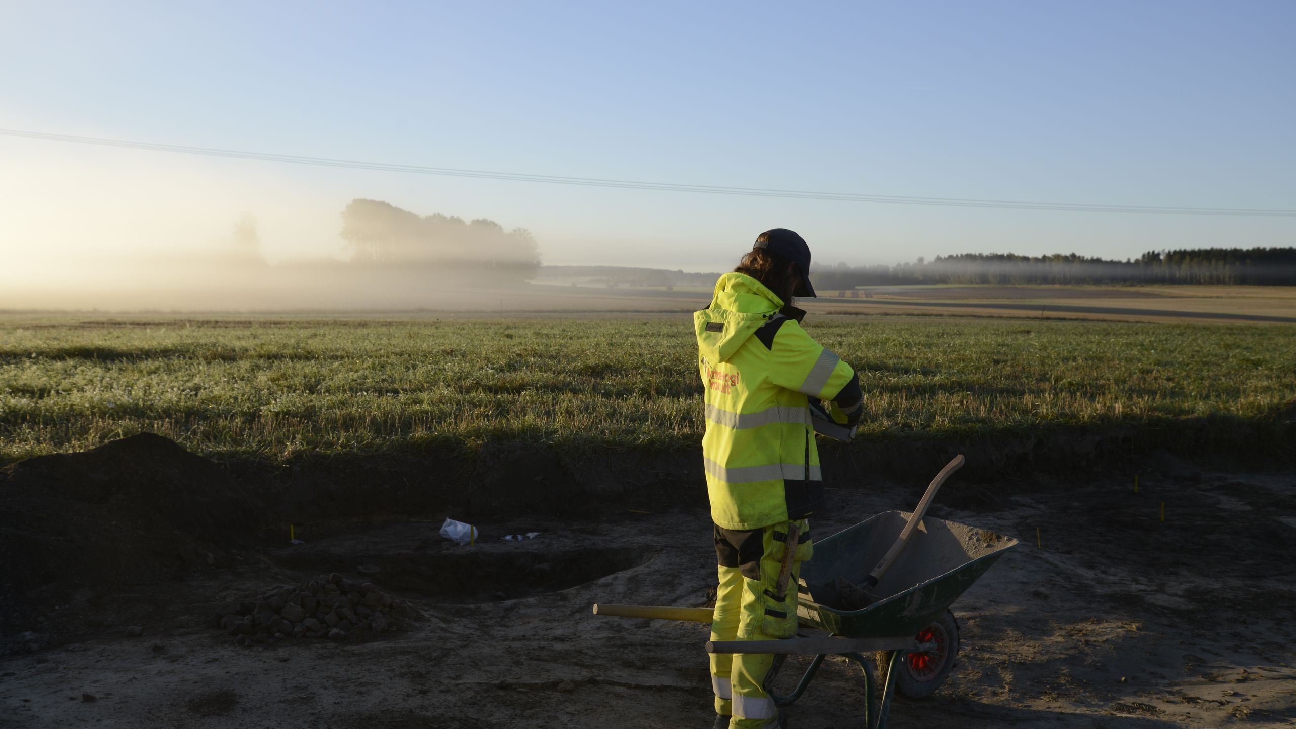 Arkeolog med skottkärra i ett dimmigt morgonfält